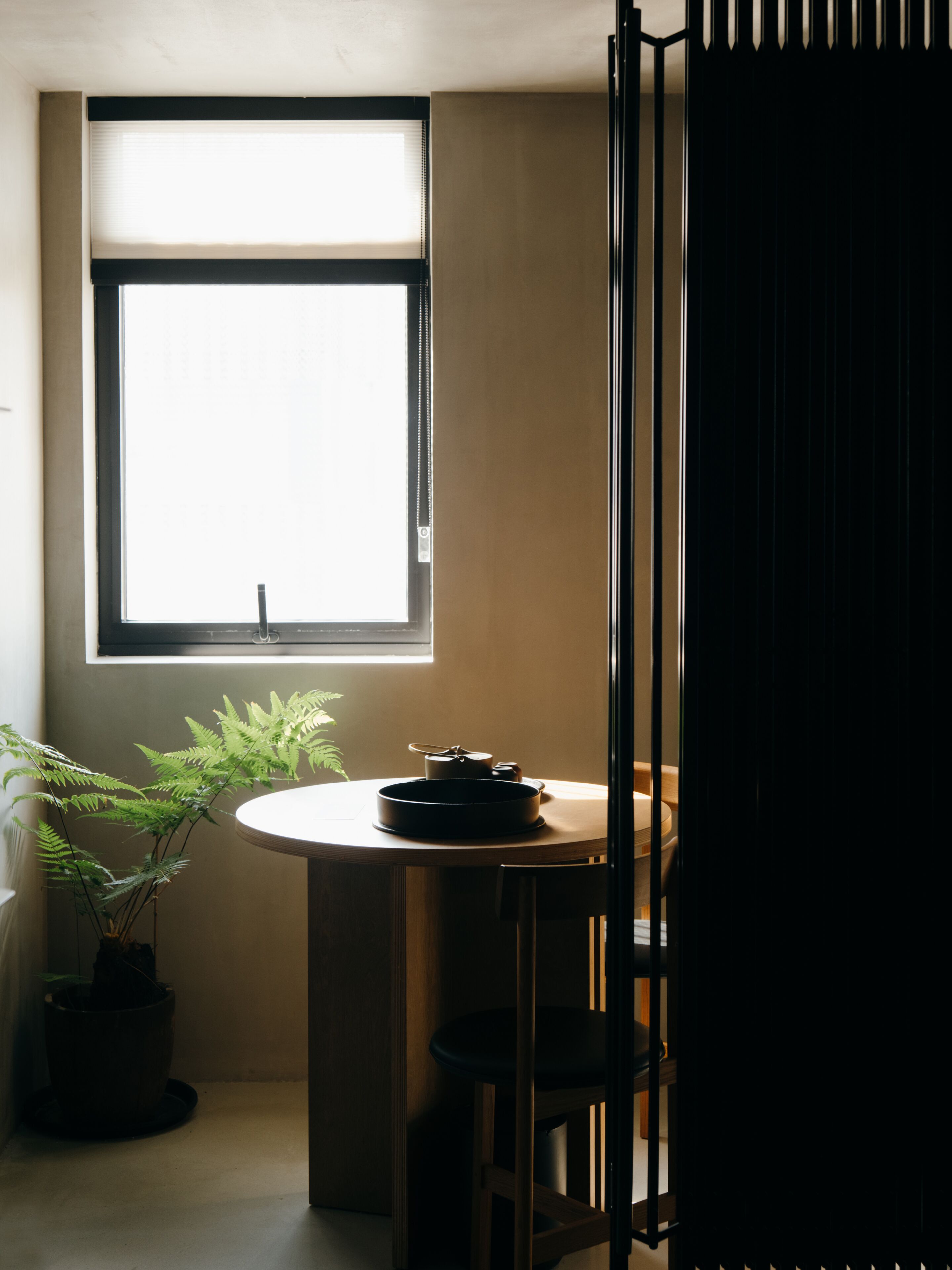 A room with a window, a round table with a black pan, and a potted plant.