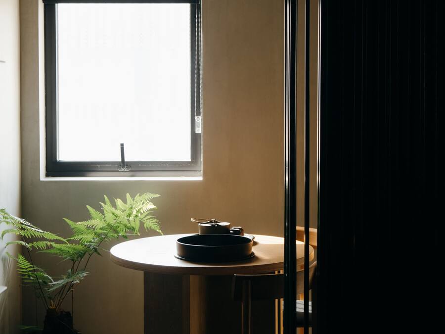 A room with a window, a round table with a black pan, and a potted plant.