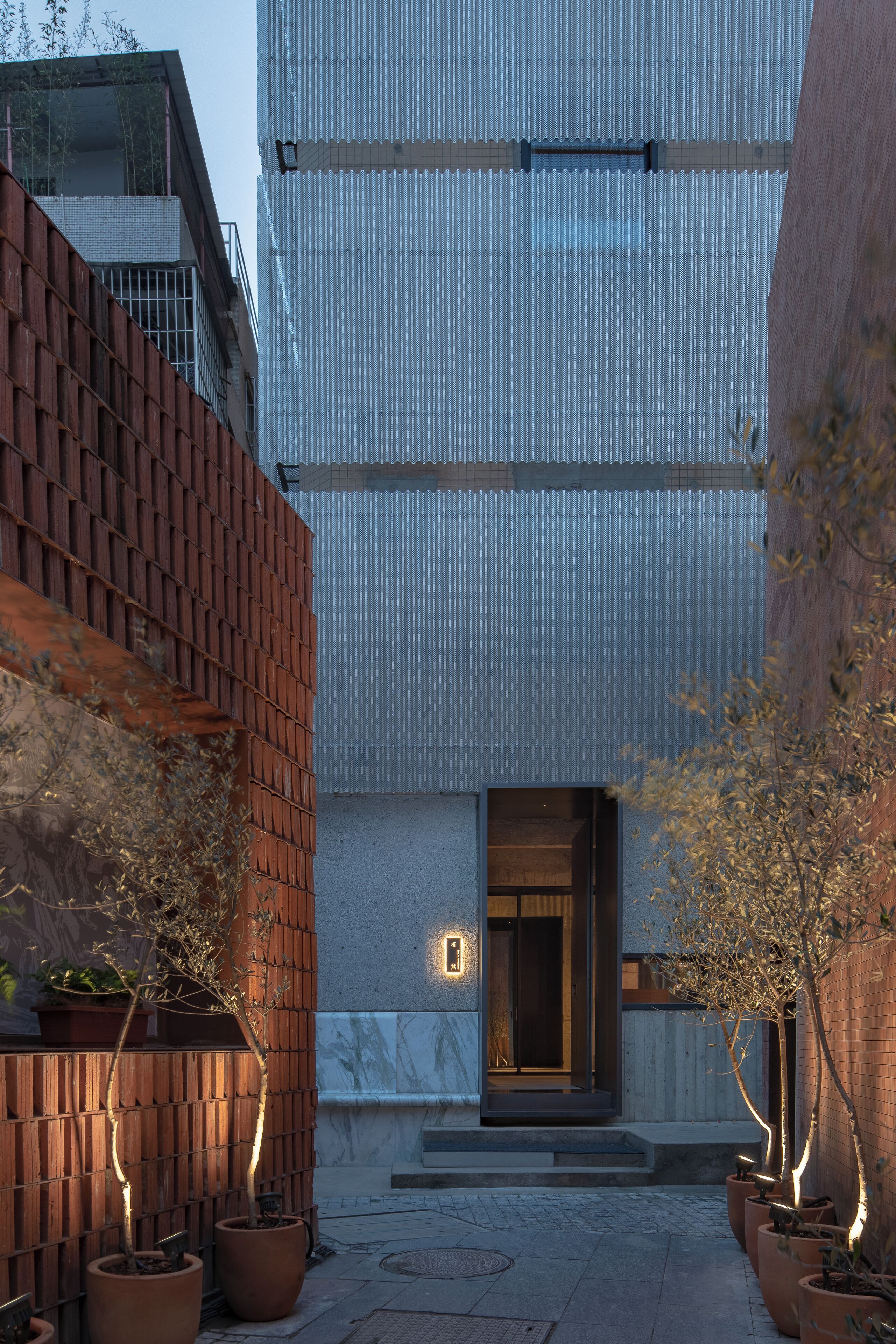 A modern building with a metal facade and a wooden fence. There are potted plants along the fence.
