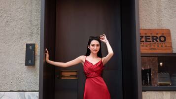 A woman in a red dress standing in a doorway with a sign reading "ZERO Waste Hotel" and a "Community Coffee Shop" sign nearby.