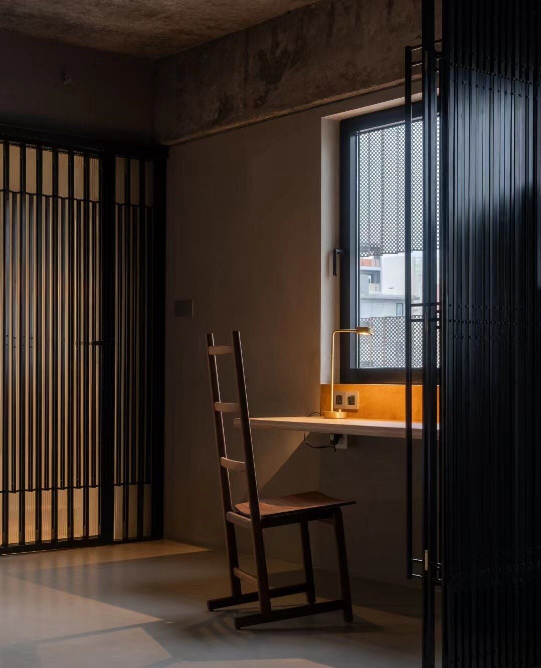 Una habitación con escritorio, silla y ventana con vista a edificios.