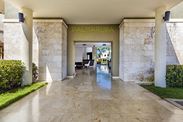 Entrada de un hotel con piso de mármol, un mostrador de recepción y una piscina visible al fondo.