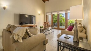 Amplia sala de estar con sofá, sillón y una mesa de centro. Un televisor de pantalla plana está montado en la pared, y hay una puerta corrediza de vidrio que da a un patio exterior.