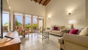 Amplia sala de estar con un gran ventanal corredero que da a un balcón, un sofá color beige, una mesa de centro y un televisor sobre un mueble de madera.