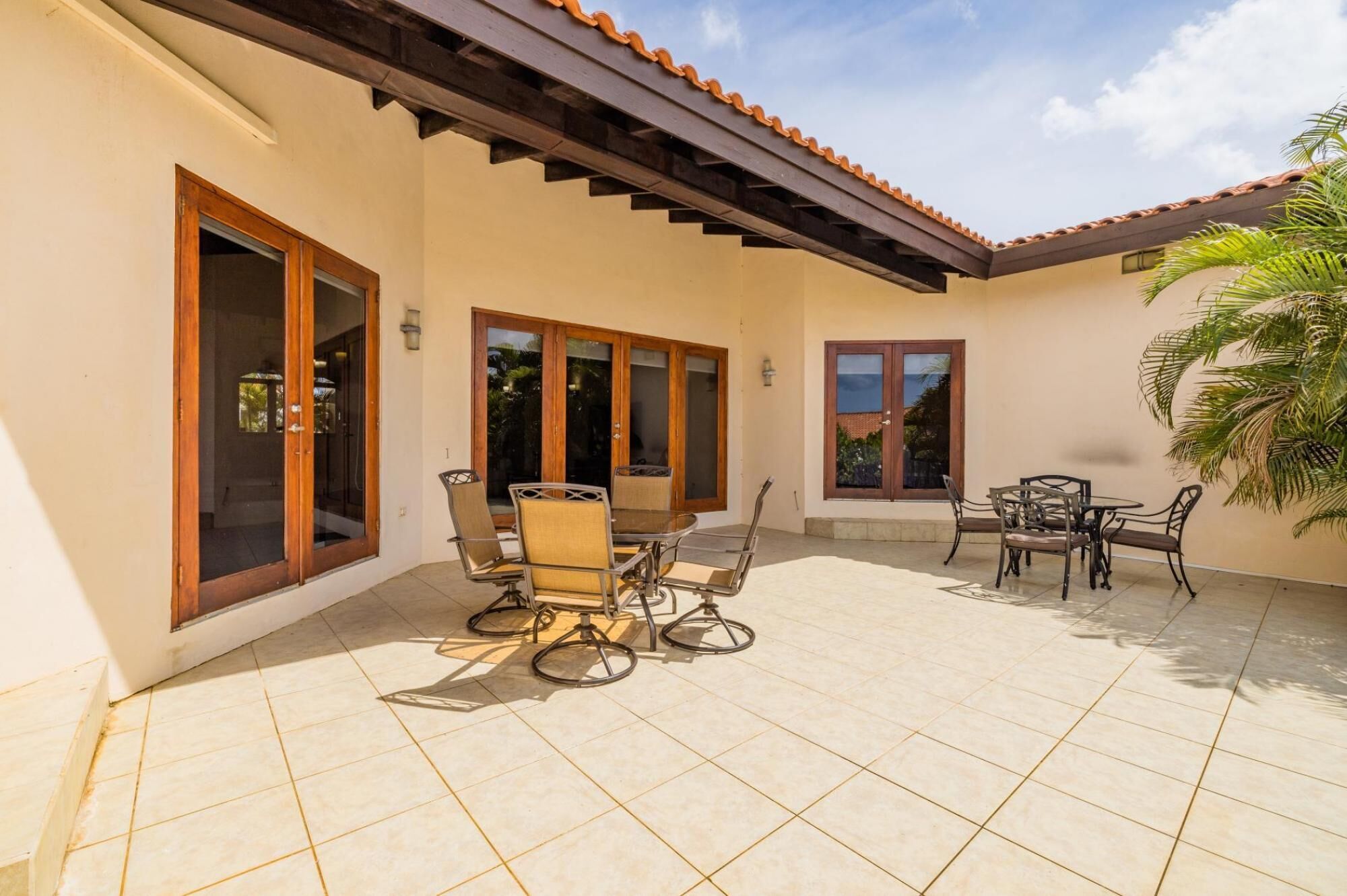 A covered patio with a dining table and chairs, large windows, and a tiled floor.