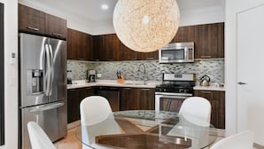 Une cuisine moderne avec des meubles en bois foncé, des appareils électroménagers en acier inoxydable, une table à manger en verre et un luminaire suspendu au design original et à la texture particulière.
