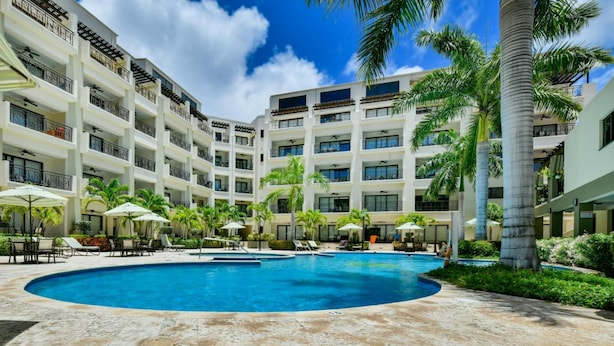 Un hôtel doté d’une piscine centrale entourée de chaises longues et de parasols, de plusieurs étages avec balcons et de palmiers.