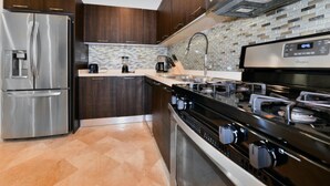 Une cuisine moderne dotée d’appareils électroménagers en acier inoxydable, d’un revêtement mural en carreaux et d’une cuisinière noire.