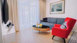 A modern living room with a sofa, a red armchair, a coffee table, and a flat-screen TV. - Rezidencia OPERA (Turcianske Teplice)