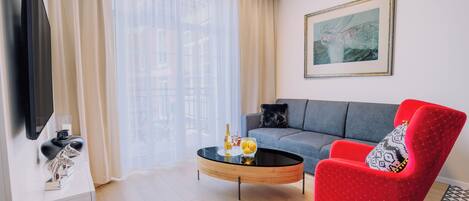 A modern living room with a sofa, a red armchair, a coffee table, and a flat-screen TV.