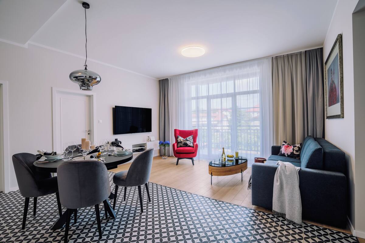 A modern living room with a dining area, a red armchair, a sofa, and a TV mounted on the wall.