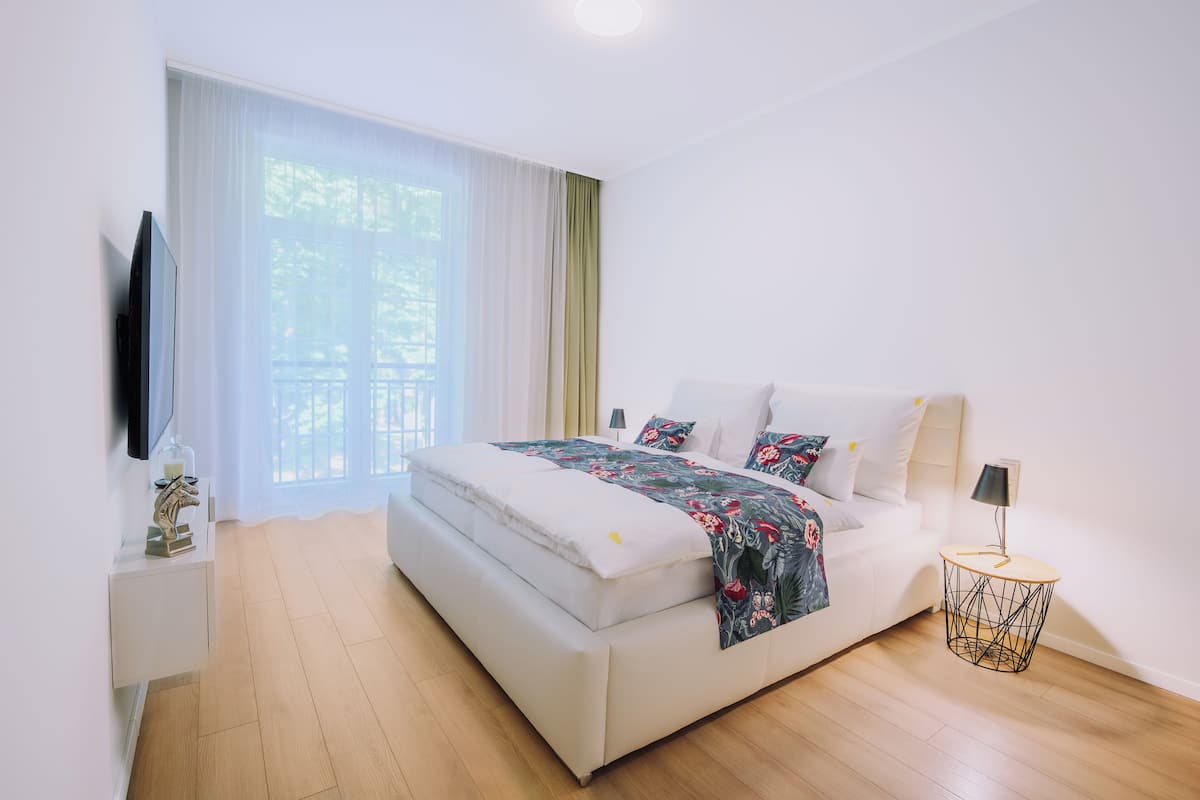 A modern bedroom with a large bed, a bedside table, a TV, and a window with curtains.