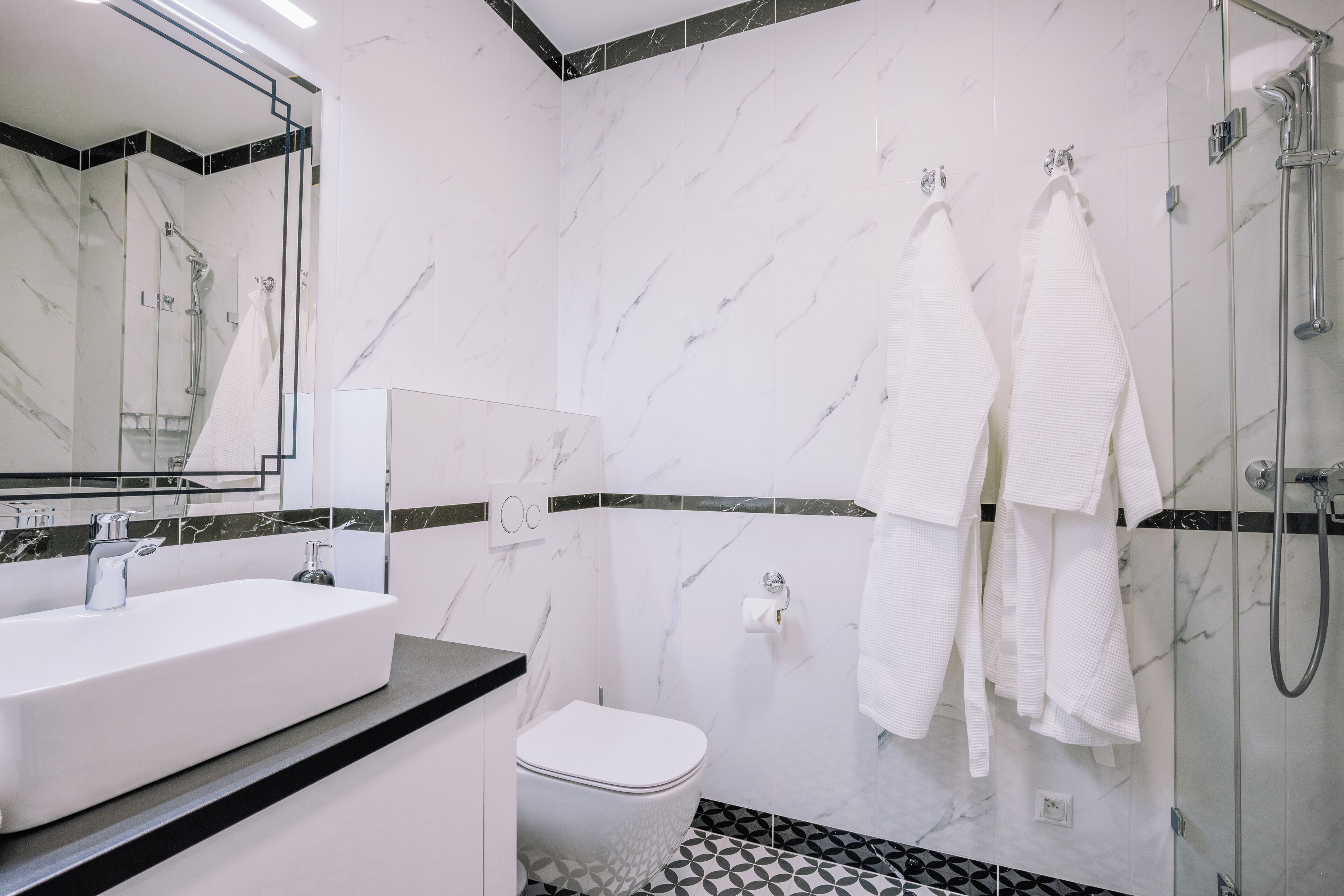 A modern bathroom with a large mirror, a white sink, a toilet, and a shower area.