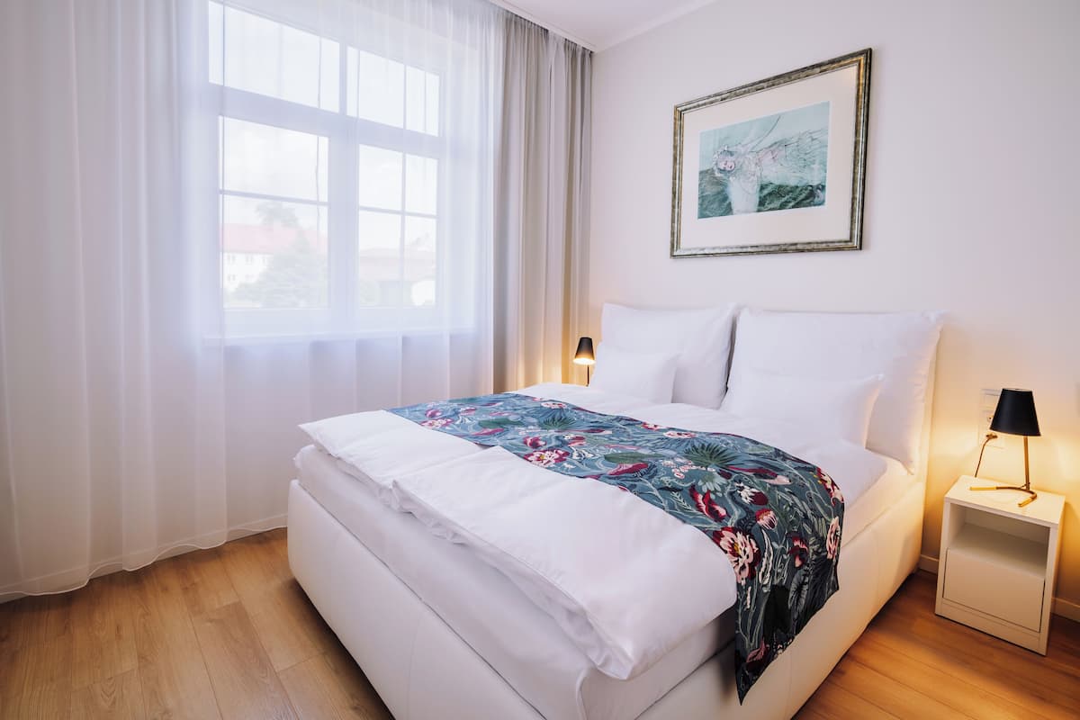A neatly made bed with white linens and a floral-patterned blanket, a bedside lamp, and a framed picture on the wall.