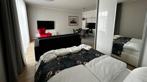 A modern hotel room with a large bed, a desk, a red chair, and a kitchen area. - Rezidencia OPERA (Turcianske Teplice)
