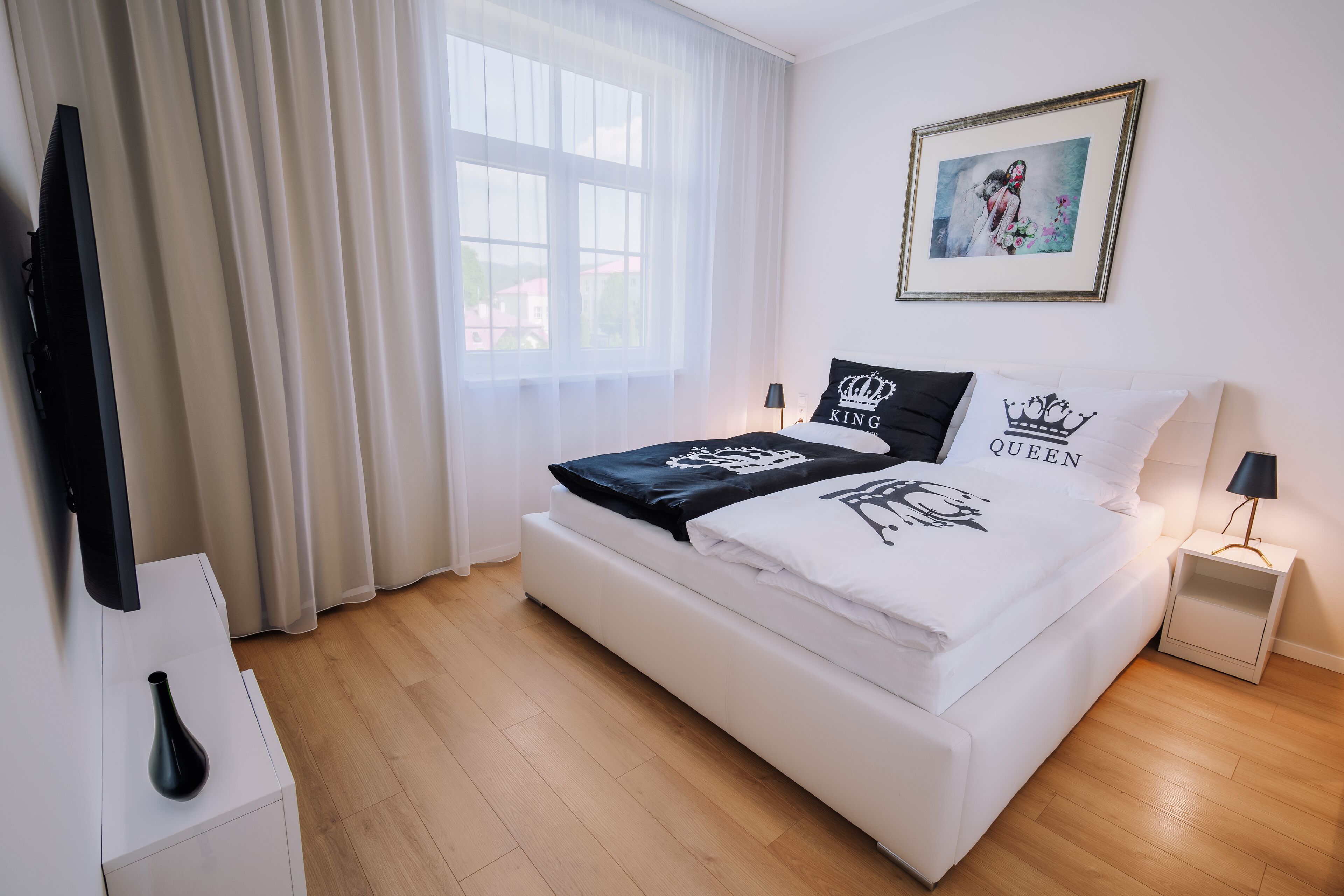 A modern bedroom with a large bed, a flat-screen TV, a vase, and a framed picture on the wall.