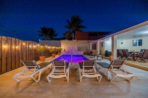 An outdoor pool area with lounge chairs and a dining table, surrounded by a wooden fence and potted plants. - 3BR Privatepool - Outdoor Dining - Great Location (Oranjestad)