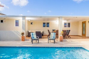 A poolside area with a pool, lounge chairs, and a table with chairs. - 3BR Privatepool - Outdoor Dining - Great Location (Oranjestad)