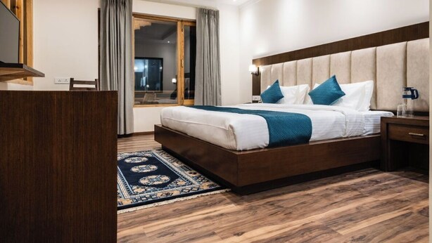 Habitación de hotel con una cama grande, piso de madera, un escritorio y vistas al exterior.