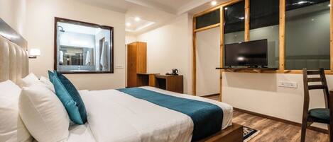 A modern hotel room with a large bed, a television, a wooden desk, and a large window.