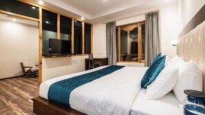 Una habitación de hotel con una cama grande, televisión, escritorio y ventana con cortinas.