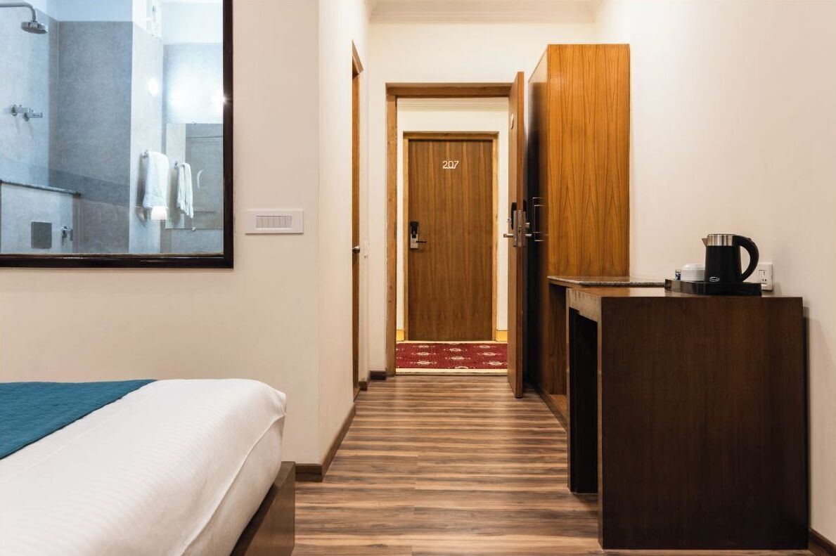 A hotel room with a bed, a wooden desk, a coffee maker, and a door marked 207.