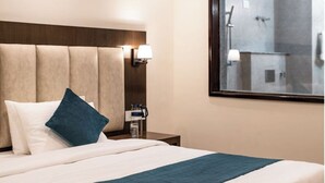 Habitación de hotel con una cama grande, cabecera, mesita de noche con lámpara y vistas a la zona de ducha.