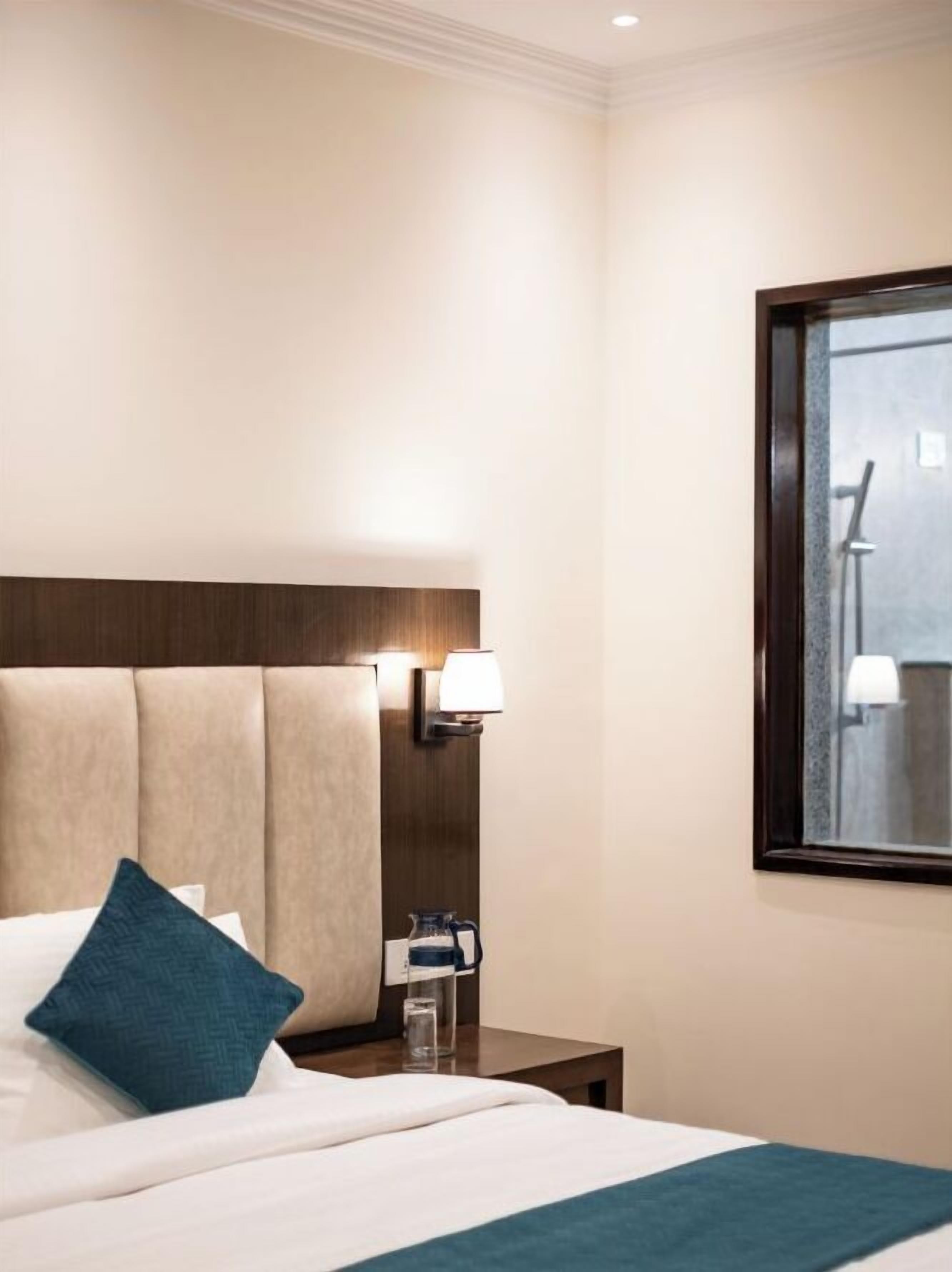 Et hotelværelse med en seng, et natbord, en lampe og et vindue.