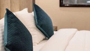 Una habitación de hotel con cama, almohadas, cabecero y lámpara de pared.