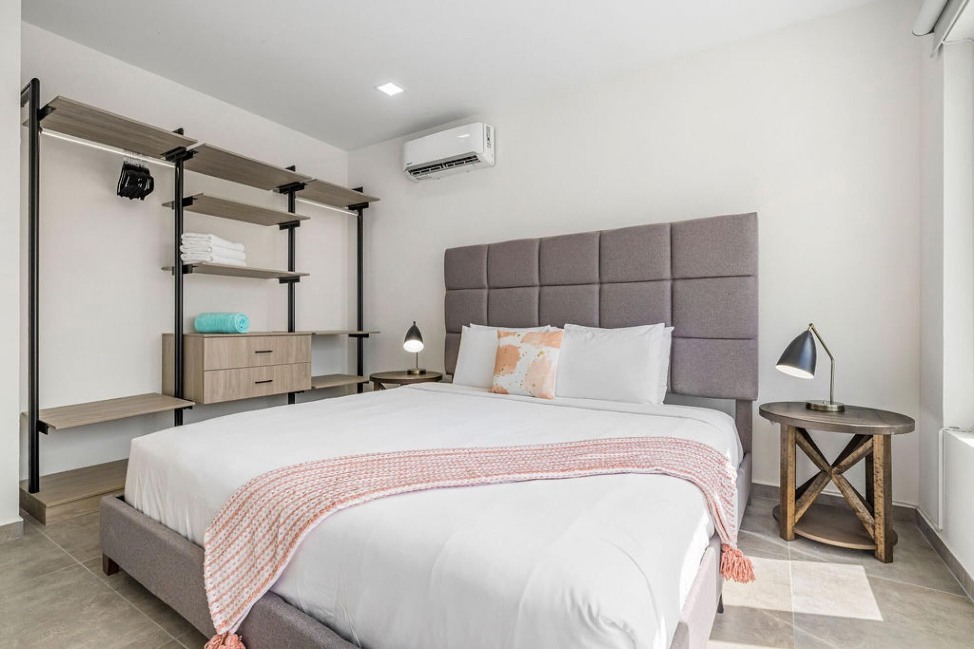 A modern bedroom with a large bed, a built-in wardrobe, a bedside table, and an air conditioning unit.