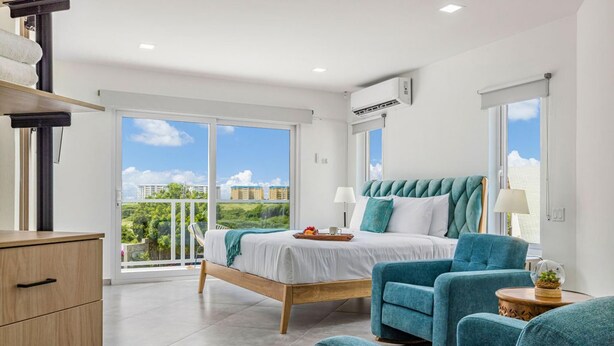 A modern bedroom with a bed, two armchairs, a wooden dresser, and a balcony with a city view. - NEW 6 Bedroom Villa 2min Eagle Beach Palm Beach (Noord)