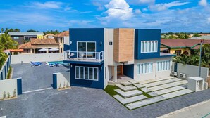 A modern two-story building with a balcony, a swimming pool, and a paved driveway. - NEW 6 Bedroom Villa 2min Eagle Beach Palm Beach (Noord)