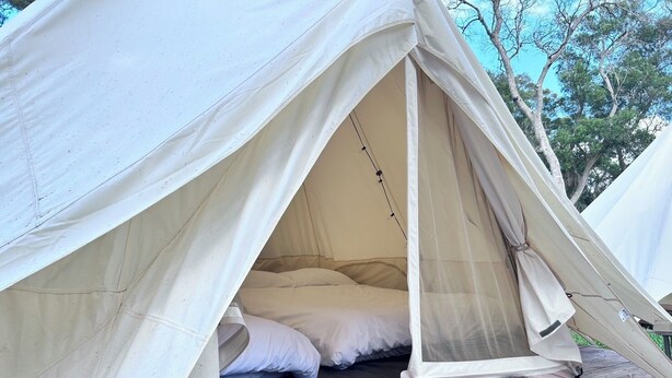 Een tent met een bed aan de binnenkant, op een houten platform gezet.
