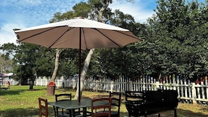 Een terras met een tafel, stoelen en een grote parasol, een barbecue en een houten terras.