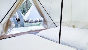 Een tent met een bed van binnen, uitzicht op de omgeving en een boom zichtbaar door de deuropening.