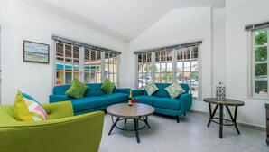Un salon lumineux avec un canapé turquoise, un fauteuil vert et une table ronde.