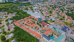 Vue aérienne d’une ville côtière, avec des quartiers résidentiels, une rue principale et un grand bâtiment équipé de panneaux solaires.