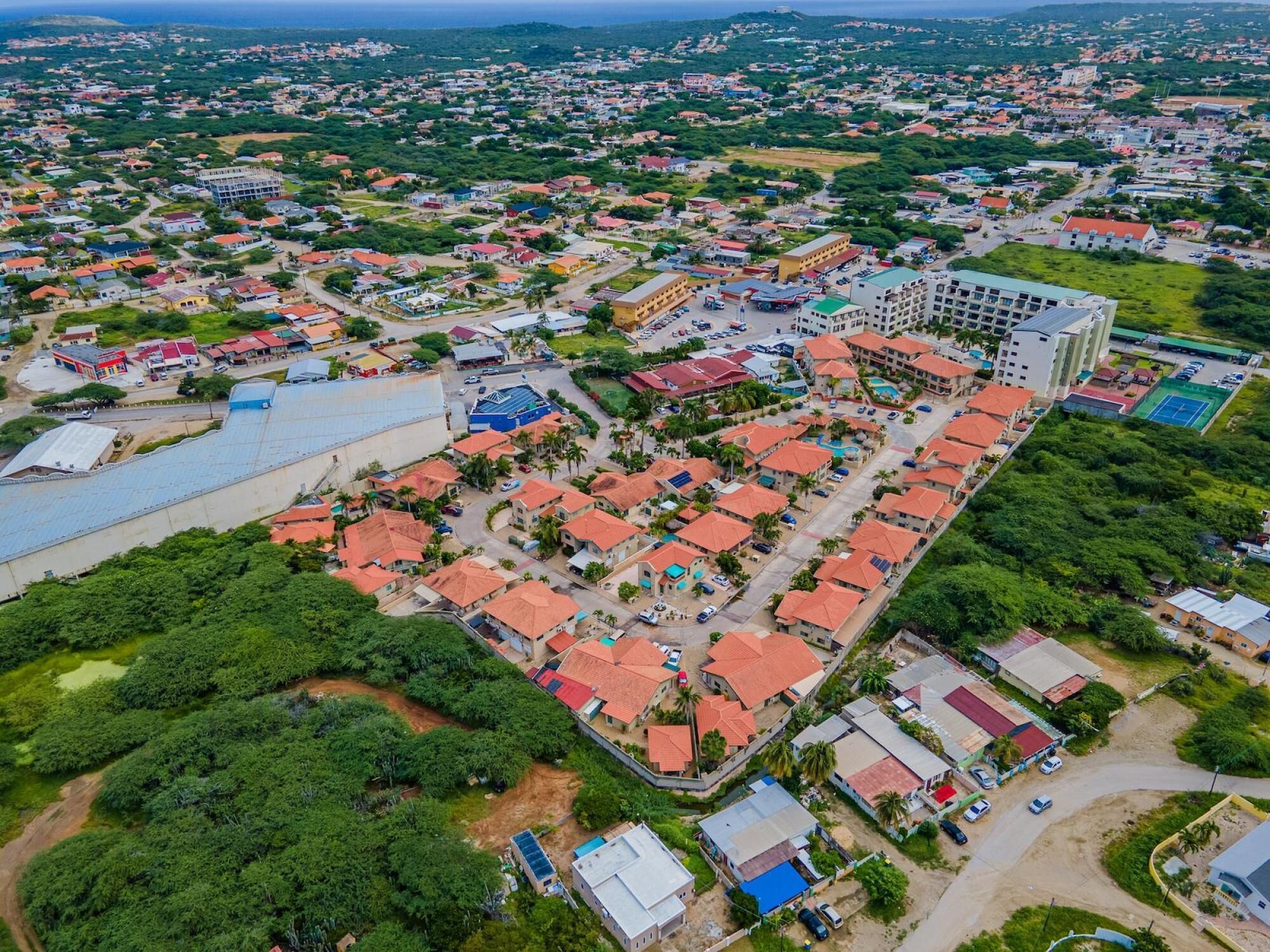 An aerial view of a residential area with a mix of single and multi-story buildings, roads, and green spaces.
