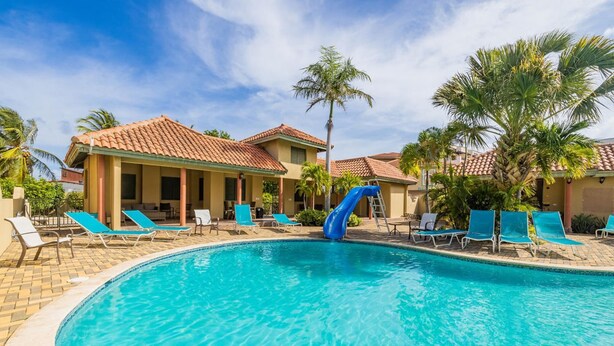 Une piscine avec un toboggan bleu, des chaises longues et des palmiers.