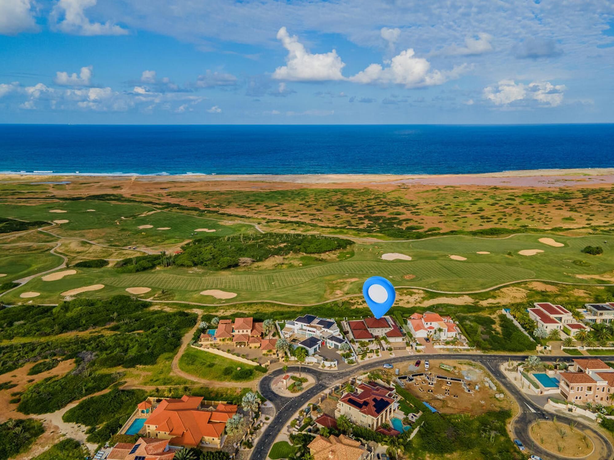 An aerial view of a coastal area with a golf course, residential buildings, and a beach.