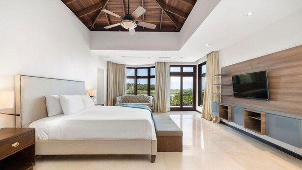 Quarto moderno com uma cama grande, um ventilador de teto, uma televisão e vista para o exterior.