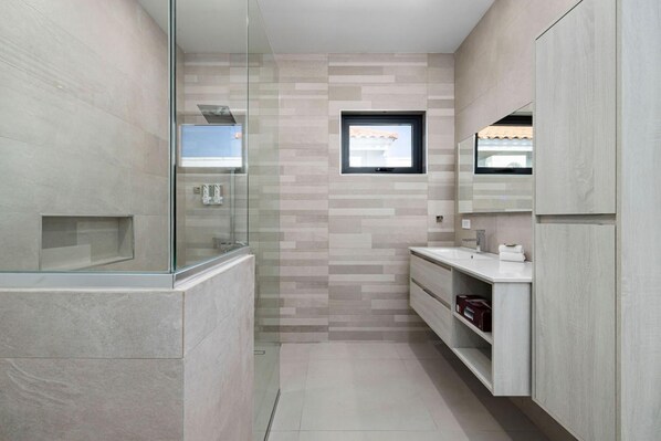 A modern bathroom with a glass shower enclosure, a built-in sink, and a window above the mirror. - Brand New Modern Villa w 3BR 2 5BA Privatepool (Noord)