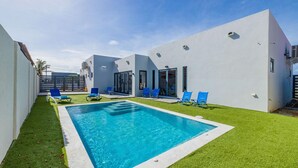 A modern pool area with a rectangular pool, surrounded by artificial grass and blue lounge chairs.