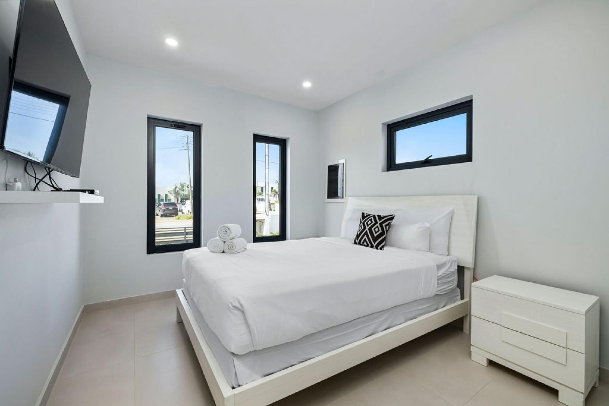 Un dormitorio moderno con una cama, un televisor montado en la pared y una ventana que ofrece vistas al exterior.