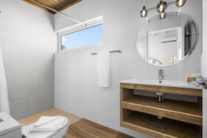 A modern bathroom with a wooden vanity, a large mirror, and a window providing natural light.