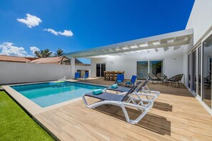 Ein moderner Poolbereich im Freien mit Holzterrasse, Liegestühlen und einer überdachten Veranda.