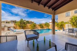 Un espace extérieur avec une piscine, des chaises longues, un barbecue et une table avec des bouteilles.