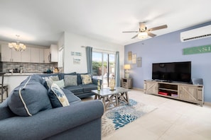 Relax in this stylish living room with a large sofa, flat-screen TV, and sliding door to an outdoor area with a pool.