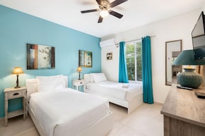 Two single beds with white bedding, a bedside table, and a ceiling fan.