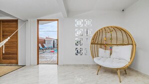 A modern interior with a wicker chair, a hammock, and a view of a pool and buildings outside. - NEW 4br3ba Villa Near Eagle Beach w Private Pool (Oranjestad)